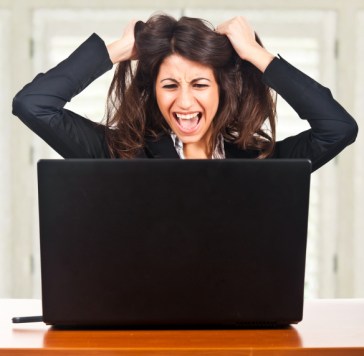 Woman sitting in front of laptop, gripping her hair and yelling