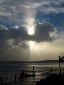 sun behind the clouds, over a calm sea