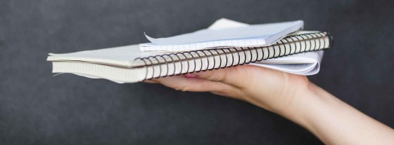 A hand balances 3 notebooks on the palm.